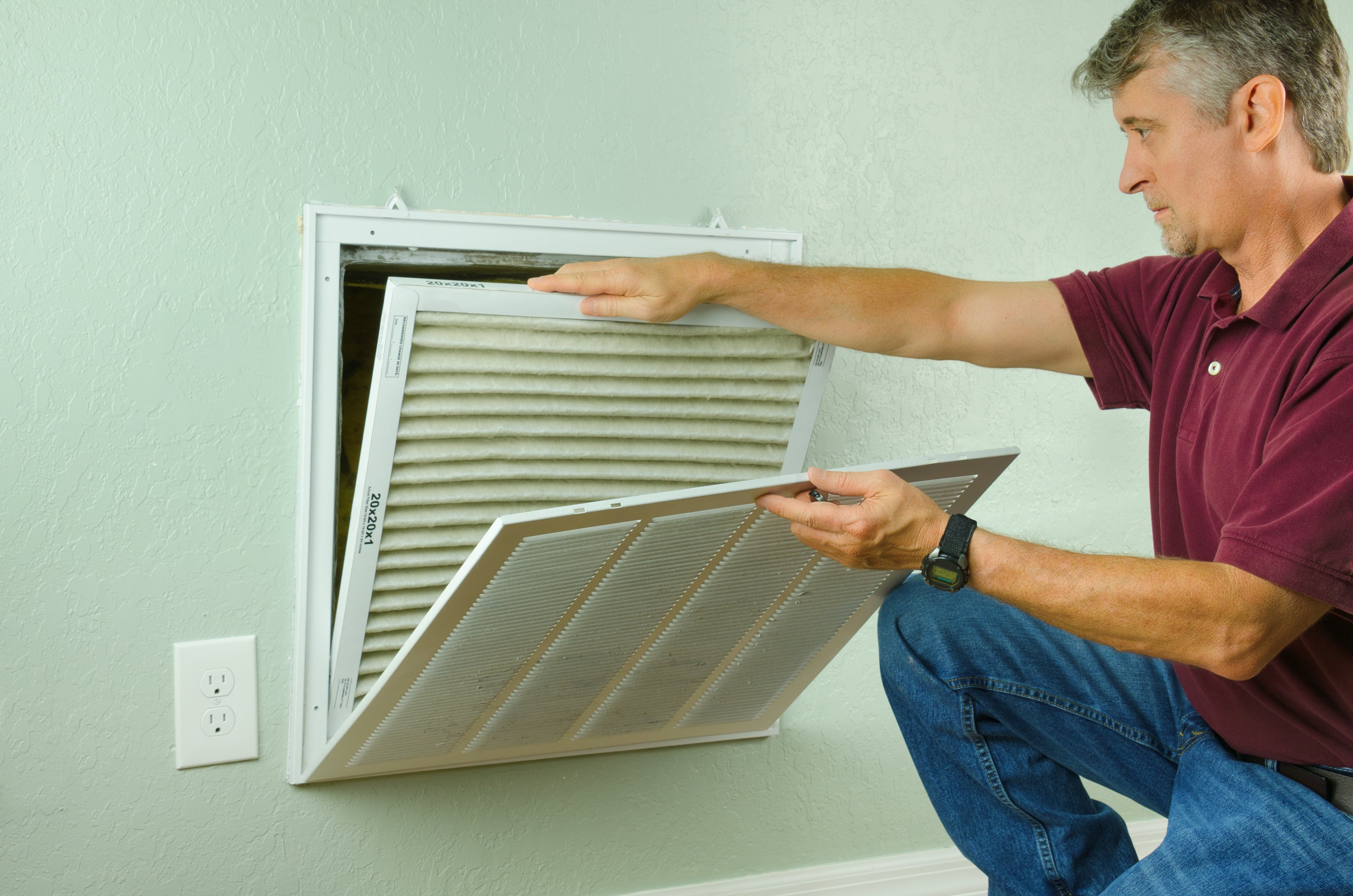 Technician removing a dirty air filter from a wall return vent